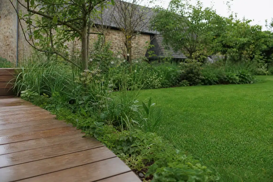 Jonction terrasse-pelouse finie : bordure plantée et joint engazonné au pied des lames, dans un jardin de l'Orne.